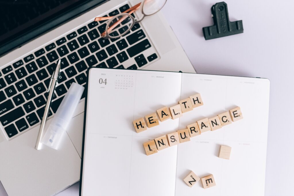 A phrase “Health Insurance” is assembled from wooden blocks on top of the pages of an opened notebook.