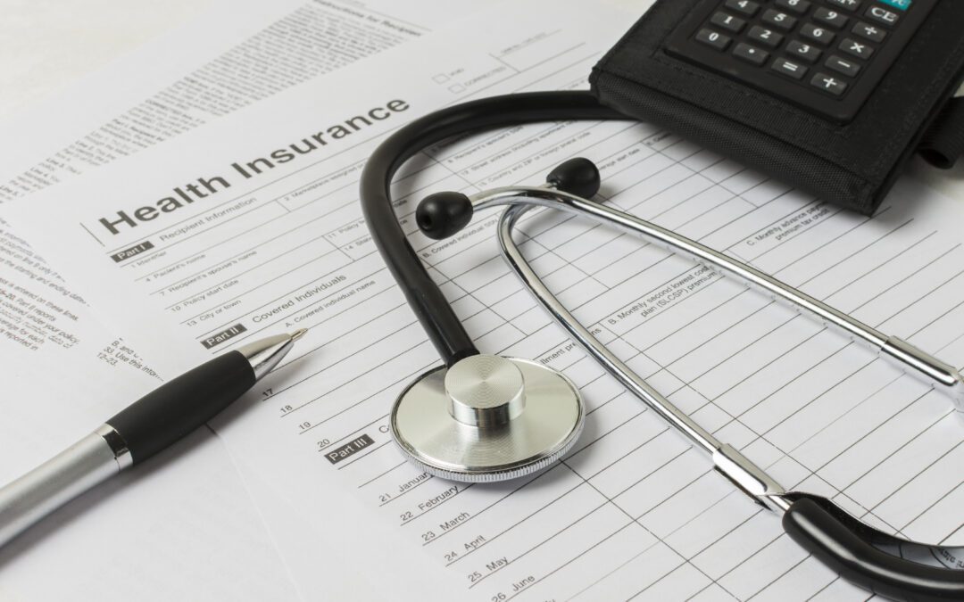 Health insurance paperwork with a stethoscope, calculator, and pen around it.